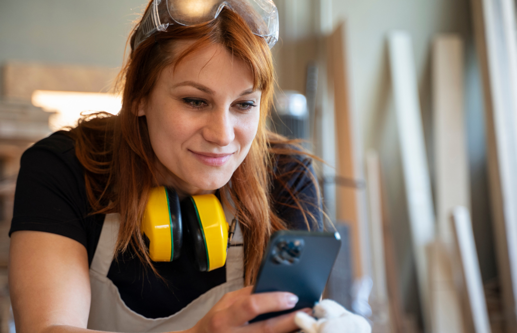 Handwerkerin mit Handy in der Hand bei der Erfassung ihrer Arbeitszeit